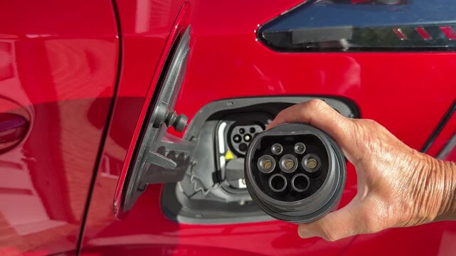 Close up of adapter plug for vehicle to load being plugged in to a type 2 charge socket on a bright red electric car