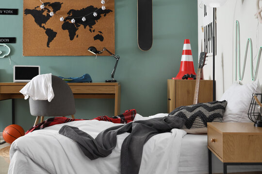 Interior of messy teenager's room with bed, workplace and lamps