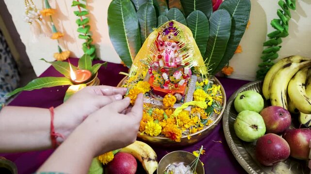 woman offering flowers to lord ganesha idol during hindu puja ceremony