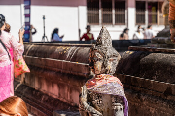 Naklejka premium Weathered female guardian figure stands within a sacred temple site surrounded by historic stone structures and cultural heritage architecture.