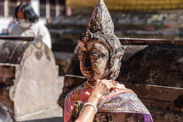 Naklejka premium Weathered female guardian figure stands within a sacred temple site surrounded by historic stone structures and cultural heritage architecture.
