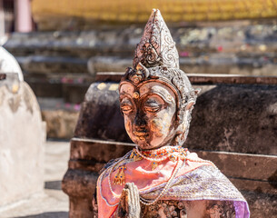 Naklejka premium Weathered female guardian figure stands within a sacred temple site surrounded by historic stone structures and cultural heritage architecture.