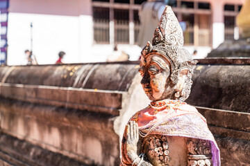 Naklejka premium Weathered female guardian figure stands within a sacred temple site surrounded by historic stone structures and cultural heritage architecture.
