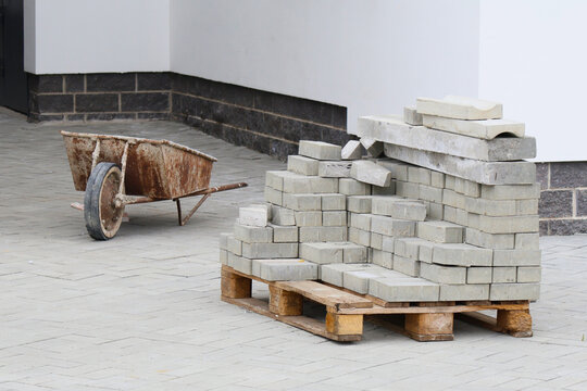 Rusted construction trolley stands idle beside a precariously stacked pile of concrete blocks on a wooden pallet. The scene evokes a moment of halted work - a quiet interlude in the rhythm of building