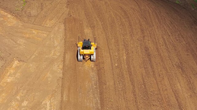 Aerial bulldozer leveling construction site soil with powerful blade pushing earth. Heavy equipment working in land grading operations, infrastructure development, industrial earthmoving workflow