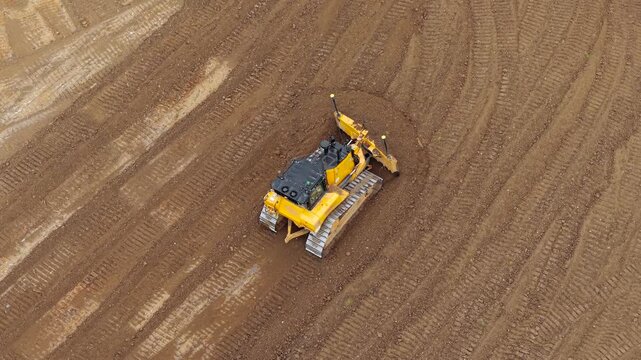 Bulldozer turning across muddy construction soil while pushing earth with front blade. Industrial site operations reflecting terrain correction, ground preparation, engineering earthworks activity