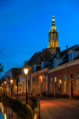 Naklejka premium Dutch canal house with street lighting on, Onze Lieve Vrouwetoren clock tower in the background, empty space, Amersfoort, Netherlands, European lifestyle