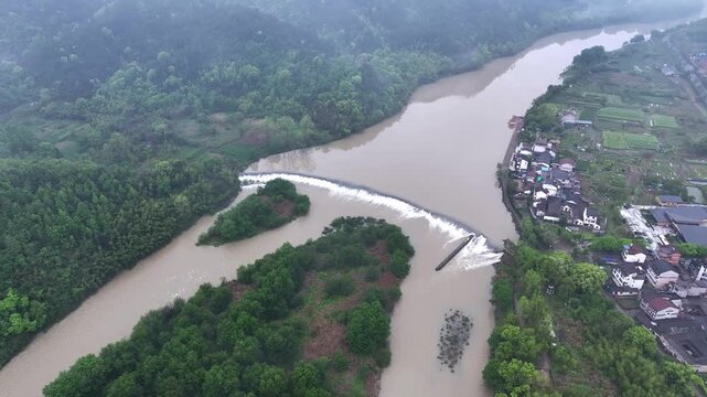 Aerial view of a river with a weir dam flanked by villages and lush green forests