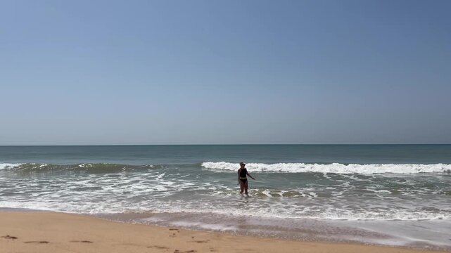 Young woman raising hands on beach. Summer holidays at tropical island. Small waves crashing on shore. Relaxation concept 