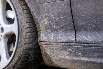 Obraz premium A car parked near a dirt road shows heavy dirt and mud on its body and tires after driving on an unpaved path under bright sunlight