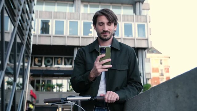 Modern man with an electric scooter checks his mobile phone while standing in an urban environment