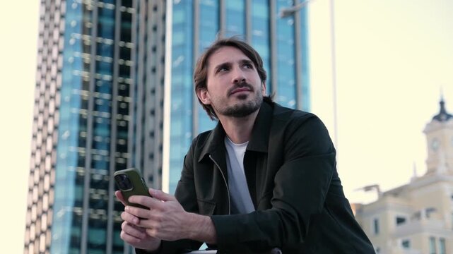 Happy man texting on his phone with modern office buildings in the background