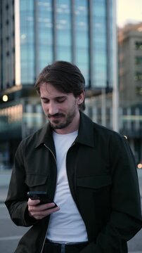 Casual handsome young man texting on his mobile phone with a modern building in the background