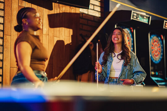 Young diverse women having fun playing pool in a bar, laughing and smiling, enjoying each other's company and leisure time