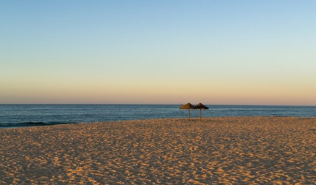 Wooden umbrellas on an empty sandy beach at sunset in low season