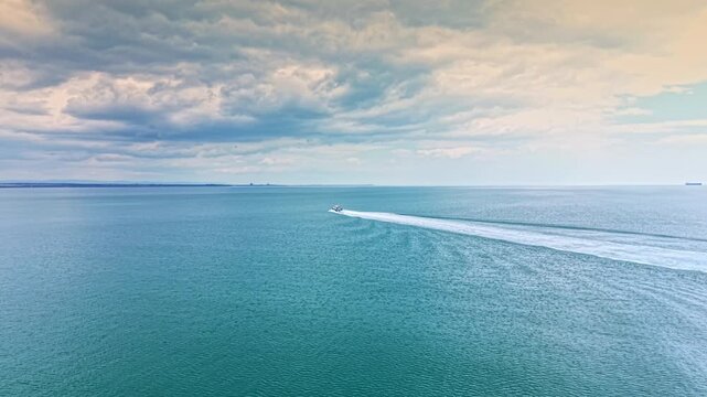 A boat travels quickly over the water as clouds fill the sky. The scene shows a horizon with distant land. The time is midday, and the water is smooth.