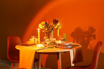 Beautiful table setting with bouquet of flowers and candles near orange wall in evening dining room