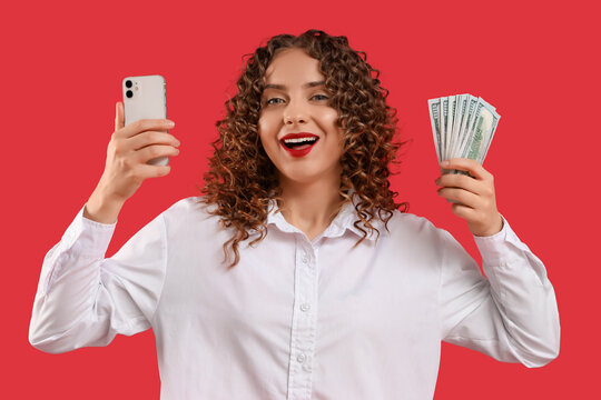 Happy young woman with mobile phone and money on red background. Sports bet concept