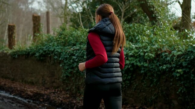 Cardio runner moving along forest pathway near green hedge in countryside setting. Middle aged female jogging outdoors strengthening muscles and boosting energy. Wellness activity supporting weight