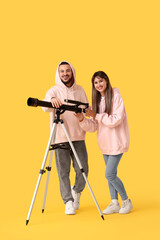 Fototapeta premium Young couple with telescope on yellow background