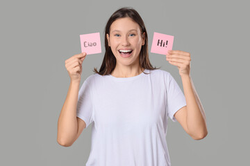 Young woman holding papers with words HI and CIAO on grey background © Pixel-Shot