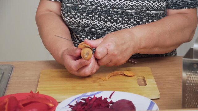 Peeling carrot with knife for cooking Ukrainian borscht. Cleaning orange root for preparing traditional soup. Removing skin from fresh carrot for making borscht recipe. Preparing vegetable ingredient