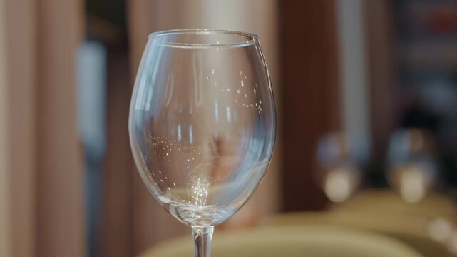Empty wine glass on table, cinematic bokeh and warm lighting creating cozy restaurant atmosphere crystal stemware catching subtle reflections and soft sparkle, sommelier nearby, blurred background