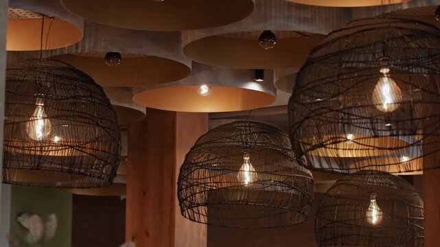 Warm woven pendant lights hanging overhead cluster of wire cage lamps with exposed filament bulbs, amber glow casting textured ceiling patterns, rustic interior and cozy lounge vibe, bartender