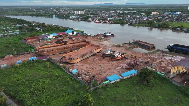 An aerial view of a river shipyard filled with barges, tugboats, and activity at an Indonesian industrial dock.