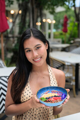 Naklejka premium Happy Thai woman at a city cafe enjoying a nutritious acai bowl during her leisure travel lifestyle.