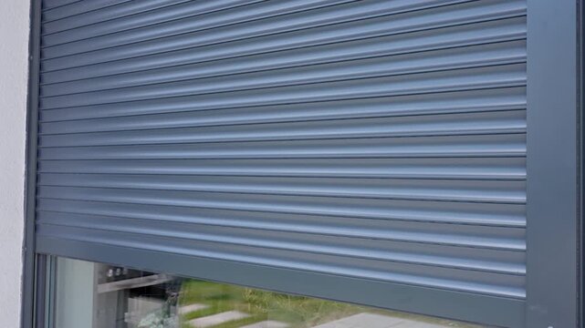 Grey automatic exterior roller shutter rises over a large glass window on a modern residential facade. Home security privacy smart home automation sun protection and window covering concepts