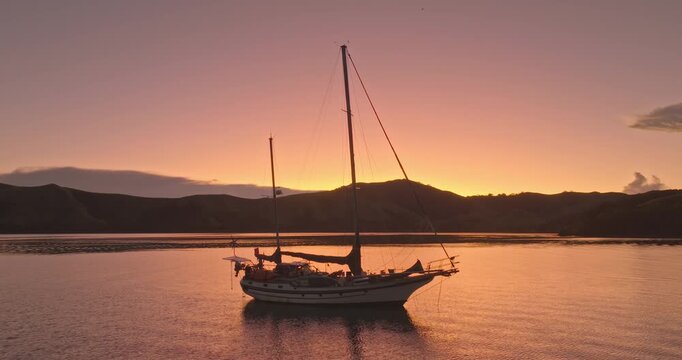 Sailing yacht floating peacefully on calm ocean waters during a vibrant sunset in the Fiji islands, reflecting warm orange and pink hues across the tranquil sky and surrounding tropical landscape