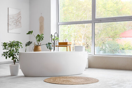 Interior of light room with white bathtub and plants