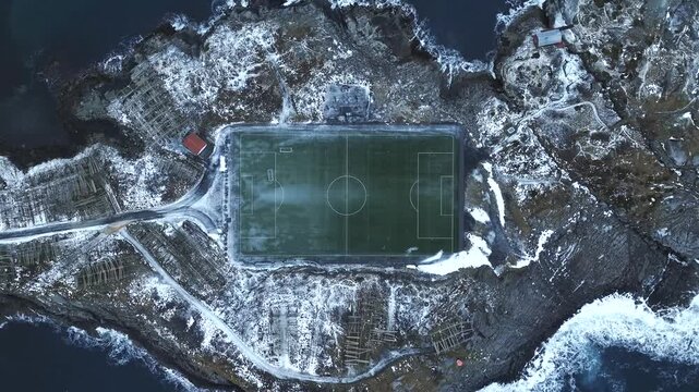 Henningsvaer stadium on Austvagoya coast in Vagan Nordland Norway lies on exposed rocky islet within Norwegian Sea with artificial turf pitch and surrounding maritime landscape, drone slow rise