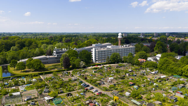 Aerial view of the KNMI building complex and radar tower surrounded by lush green trees and community allotment gardens in De Bilt, Utrecht, Netherlands.