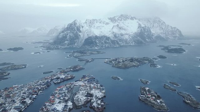 Henningsv&aelig;r in V&aring;gan, Lofoten Islands, Norway spans skerry islands on strandflat within Vestfjorden basin with Heim&oslash;ya core and Austv&aring;g&oslash;ya massif likely V&aring;gakallen as drone slides right and tilts down