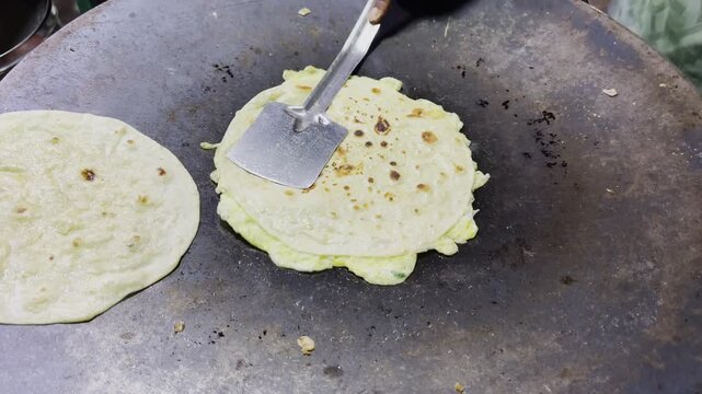 Fresh omelet being flipped on a hot cooking pan beside flatbread with rustic kitchen texture, street food preparation scene and traditional cooking atmosphere!