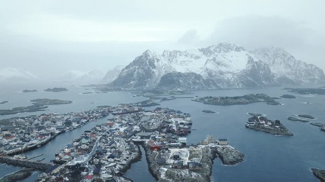 Henningsv&aelig;r in V&aring;gan, Lofoten Islands, Norway sits on strandflat within glacial fjord basin showing skerry network, harbor layout and alpine peaks in Precambrian terrain, drone parallax orbit