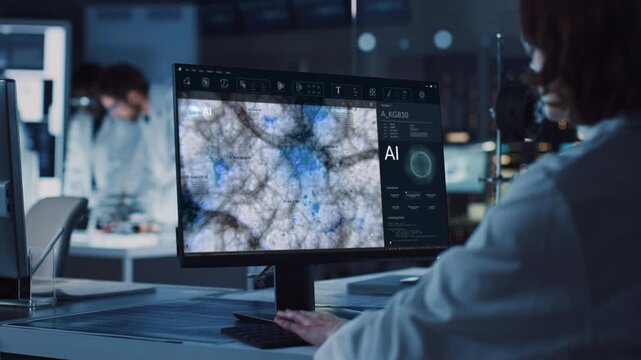 Female Scientist Analyzes AI Microscopy Data on a Computer in a High-tech Biotech Lab, Mapping Cellular Patterns to Guide Diagnostic Research While Colleagues Work Nearby. Over-the-shoulder Shot.