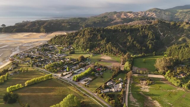 Drone view of coastal village of Marahau at edge of Abel Tasman National Park during beautiful golden hour sunrise in New Zealand. Aerial