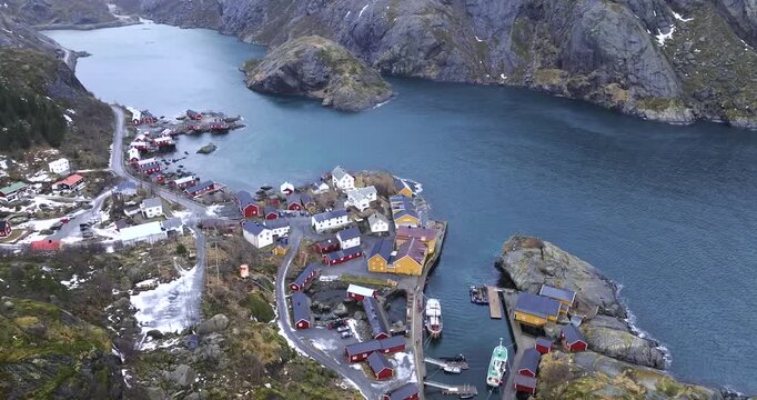 Henningsv&aelig;r in V&aring;gan, Lofoten Islands, Norway shows Heim&oslash;ya harbor basin with marina docks, main street axis from quay and Austv&aring;g&oslash;ya alpine ridge as drone parallax orbit reveals settlement