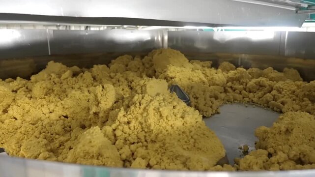 Industrial mixing blade stirring and kneading large batch of dough in commercial food processing equipment