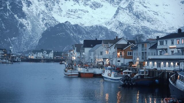Henningsvaer in Vagan Nordland Norway faces Vestfjorden with fishing vessels and quay houses glowing at blue hour below Austvagoya peaks creating serene postcard scene, static shot
