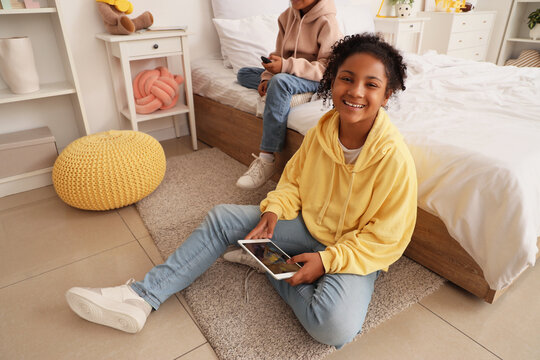 Cute happy African-American children watching cartoons on TV and tablet in bedroom at home