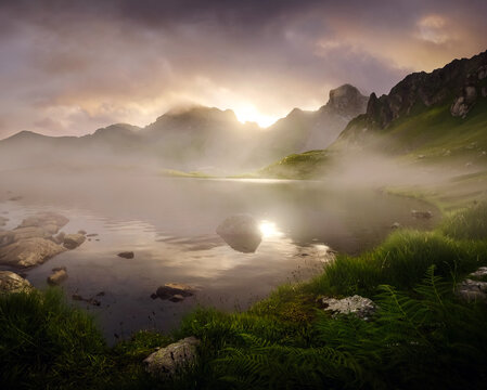 Mountain lake reflecting sun through morning fog
