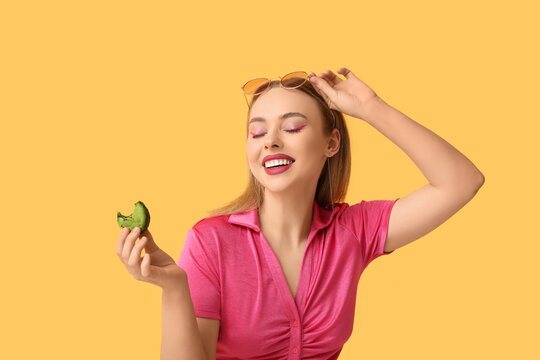 Happy young woman with green sweet macaroon on yellow background