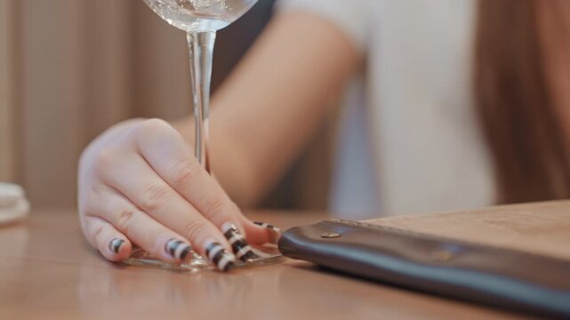 Chic lady delicately taps glass at cafe. Refined woman with polished nails raises wine glass quietly. Sophisticated individual in casual setting gently gestures with wellmanicured hand