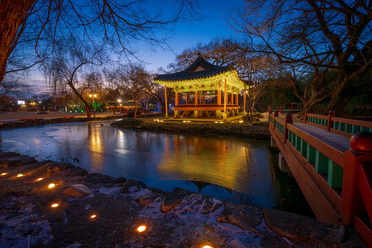 Serene twilight view of the illuminated Gwanghallu Pavilion overlooking a calm pond surrounded by bare winter trees and glowing ground lanterns in Namwon.