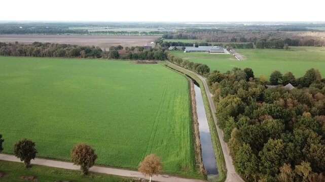 peaceful aerial drone video gliding over a quiet rural landscape, featuring a ditch with beautiful cloud reflections in the still water, surrounding farmland and arable fields, and a tree-lined road