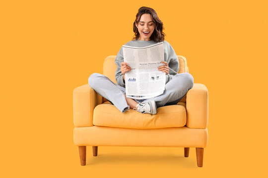 Young woman reading newspaper in armchair on yellow background